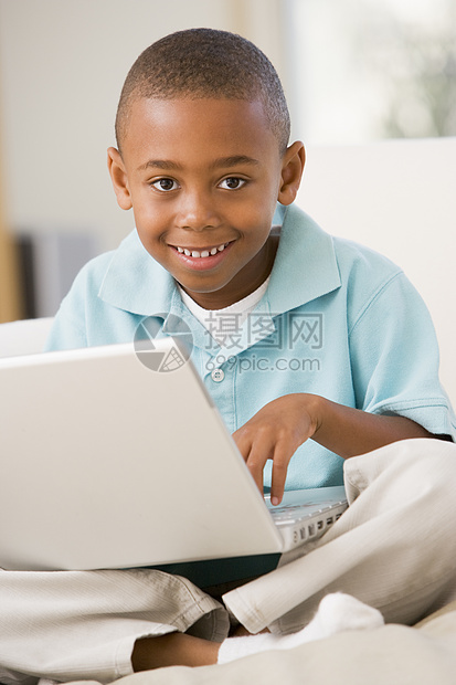 在客厅的年轻男孩带着笔记本电脑微笑图片