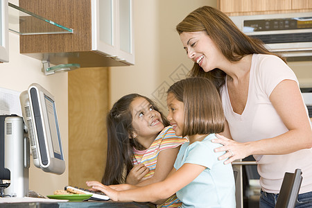 女人和两个年轻女孩在厨房里 带着电脑微笑的笑容家长孩子三个人冲浪女士孩子们妈妈帮助拉丁女性图片