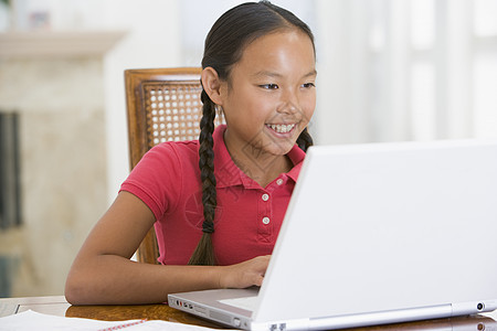 餐厅里带着笔记本电脑的年轻女孩微笑着冲浪客厅孩子技术女性桌子互联网孩子们监督家庭作业图片