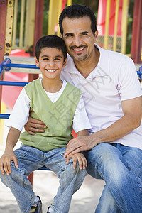 父亲和儿子坐在操场结构上笑着微笑父母孩子孩子们男士情绪拥抱小学生公园中年身份图片