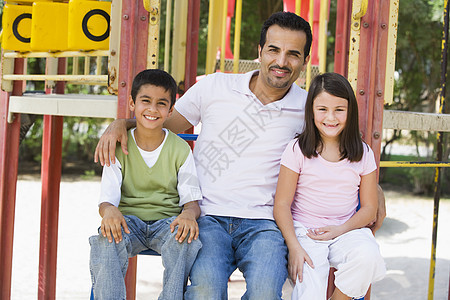 父亲和两个孩子坐在操场结构上微笑着笑图片
