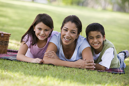 母亲和两个小孩在公园户外露着野餐微笑家长偏移角父母篮子水平孩子餐垫后代妈妈们种族图片