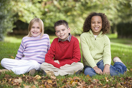 三名儿童坐在户外微笑着笑容阶段种族孩子女孩年龄树叶朋友们男孩们公园情绪图片