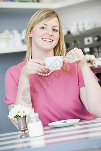 坐在桌边的年轻妇女食物饼干软垫沙发金发女郎饮料浴衣时间杯子棕色图片