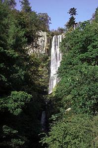 威尔士垂直瀑水石头森林树木雌蕊绿色天空苔藓雷神岩石蓝色背景图片