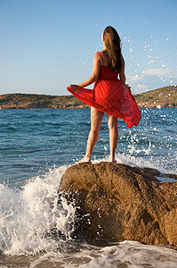 美丽的女孩在海浪中飘荡气候裙子海滩飞溅幸福日落自由女性石头享受图片