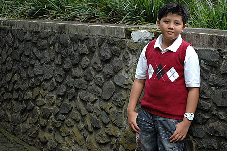 年轻男孩站在岩石墙边站立背景图片