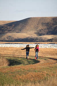 两名女孩在萨斯喀彻温的风景地带沿堤道跑动乡村孩子们避难所活动跑步农村女孩们图片
