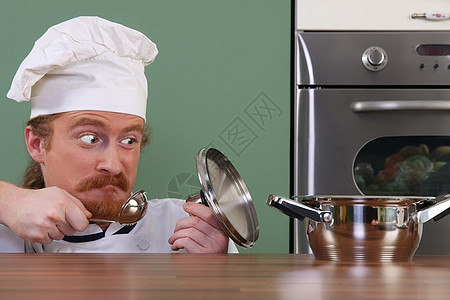 有趣的年轻厨师 奇怪地看着锅职业汤匙烹饪衣服服务勺子餐具食物盘子男人图片