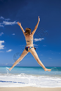 女人在海滩上跳跃闲暇身体太阳蓝色成人天空海洋天堂喜悦乐趣图片
