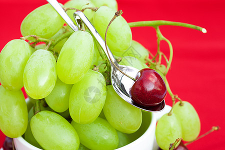 红背景的勺子中的葡萄和樱桃图片