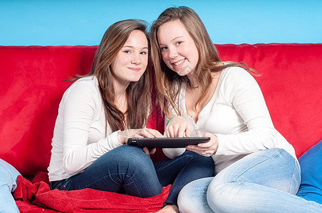 快乐的青少年在家里沙发上使用平板电脑家庭金发女郎喜悦药片金发朋友们两姐妹女孩友谊微笑图片