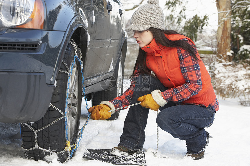 妇女把雪链锁在汽车轮胎上季节女性防滑链场景水平司机驾驶下雪围巾天气图片