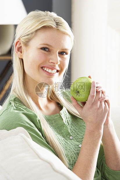 在家吃苹果时在沙发上放松妇女金发女郎客厅金发水平微笑女性成人享受饮食健康图片