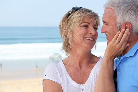 海滩上一对夫妇感情休息微笑女性展示老年爱抚假期情侣金发图片