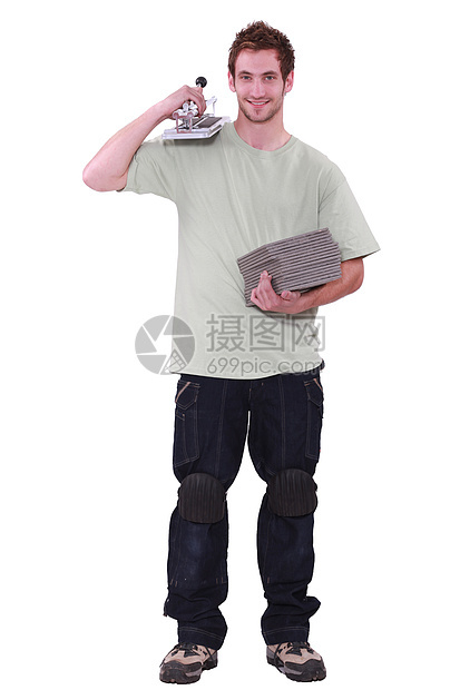 一个年轻男子拿着瓷砖和一个瓷砖切割机图片