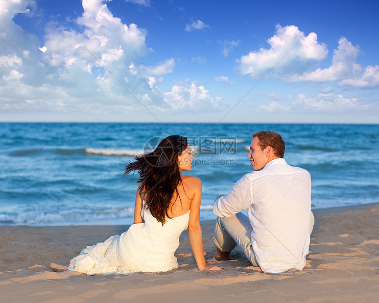 在蓝沙滩上坐着女性成人庆典婚姻男人男性裙子蜜月波浪支撑图片