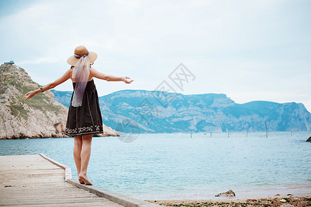 女孩在泊位上摆姿势山脉海岸女性赤脚假期裙子海滩闲暇场景青年图片