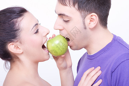 双唇间有绿苹果的年轻夫妇乐趣水果女士女孩黑发男朋友女性食物家庭女朋友图片