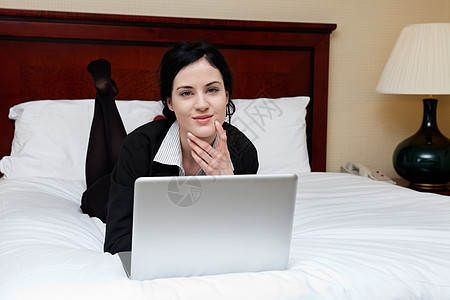 女性行政主管在用笔记本电脑床铺上躺着女孩枕头商务商业旅馆微笑说谎女士旅行酒店图片