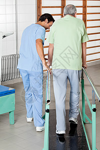 男性治疗师协助老年男子走在支持和扶助下图片