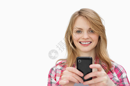 微笑的女人在看照相机时使用手机 (笑)图片