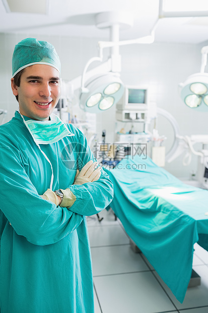 带着双臂的外科医生笑着跨过监视器手术男性操作手术室男人卫生制服面具微笑图片