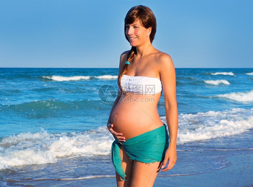 美丽的孕妇在蓝沙滩上行走妈妈分娩海滨波浪女孩泳装母性支撑家庭幸福图片