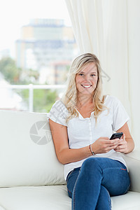 一个微笑着的女士 拿着她的手机 当她坐着看着C背景图片