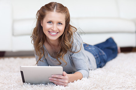 微笑的女人用她的平板电脑在地板上图片