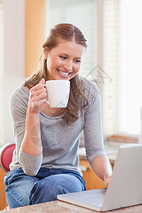 微笑的女人在打笔记本电脑时享受咖啡图片