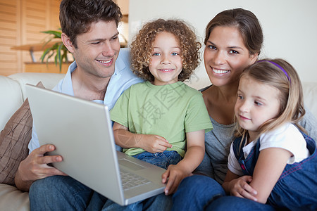 使用笔记本电脑微笑的家庭乐趣享受女士技术长椅混血压痛童年父亲女孩图片