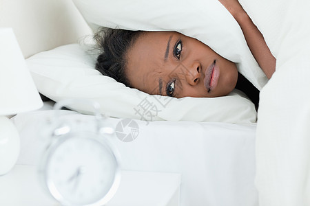 疲倦的女人在闹钟响时遮住她的耳朵图片