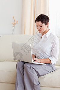 坐在沙发上拿着笔记本电脑的迷人女人图片