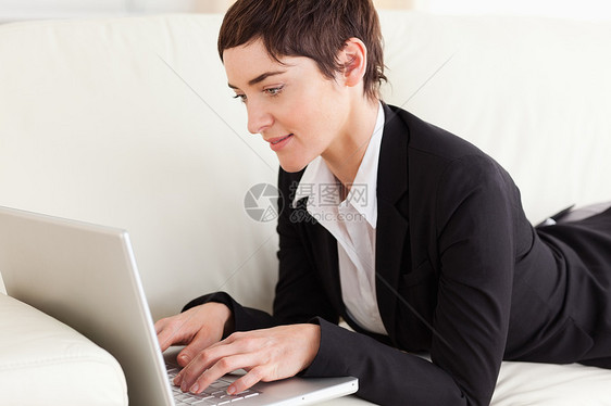 用笔记本电脑躺在沙发上的迷人女商务人士图片