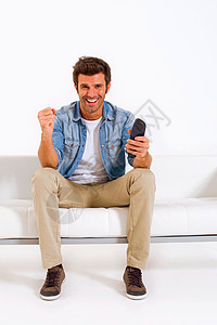 单身男子在沙发上看电视休闲装客厅热情成年人手势长椅牛仔裤微笑男人成人图片