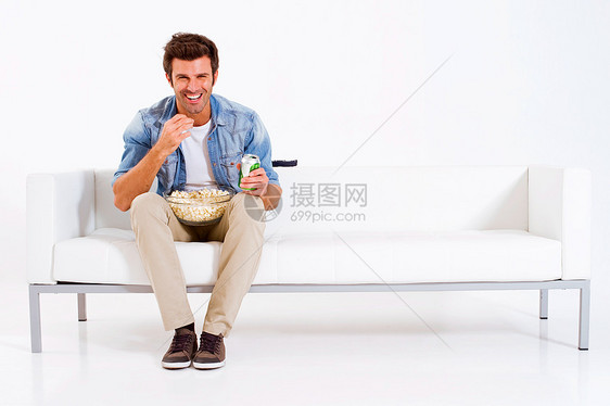 单身男子在沙发上看电视零食男人饮料微笑休闲装牛仔裤成人客厅成年人长椅图片
