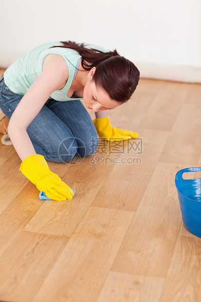 漂亮的红头发女人在跪下时打扫地板图片