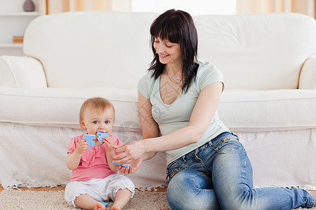 迷人的女士坐在A座上 抱着她的婴儿在她的怀里玩具沙发喜悦微笑父母地毯闲暇生活休息室房间图片