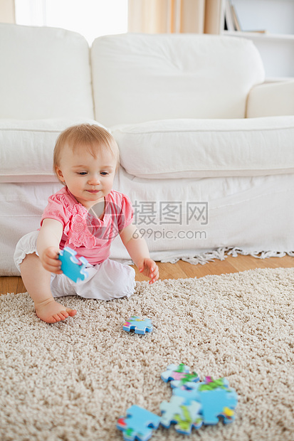 可爱的金发宝宝在玩拼谜游戏的同时坐着地毯休息室女孩房间家庭喜悦沙发白色儿子图片