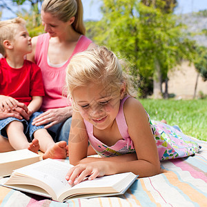 专注的金发金发女孩在和她的F去野餐时看书蓝色阅读公园儿子母亲女儿享受足球太阳家庭图片