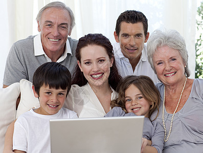使用笔记本电脑坐在沙发上的家庭肖像儿子女孩男人金发互联网祖父祖母男性女士姐姐图片
