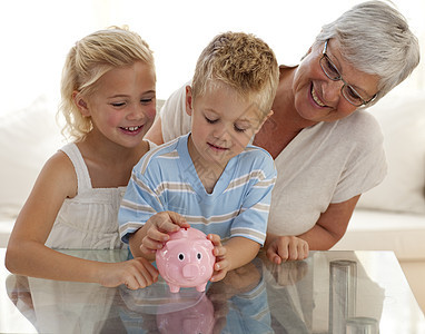祖母和孩子在小猪银行存钱硬币货币男生微笑储蓄孙女财富裙子商业小猪图片