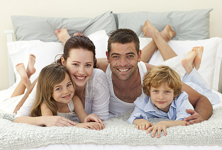 幸福的一家人躺在床上 对着镜头微笑图片
