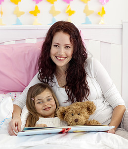 微笑的母亲和女儿在床上阅读图片