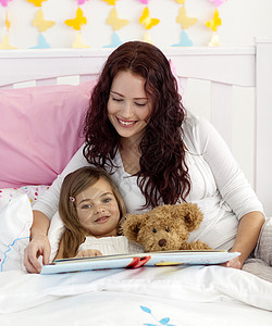 母亲和女儿在床上阅读微笑幸福卧室孩子乐趣女士家庭金发蓝色女孩图片
