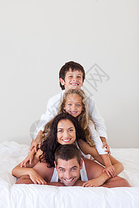 躺在床上的微笑的家庭感情兄弟拥抱父亲女儿乐趣家长女孩女士孩子图片