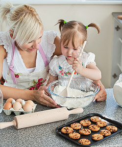 微笑的女人和女儿一起做饼干幸福勺子成人手工家庭围裙女孩快乐兄弟面粉图片