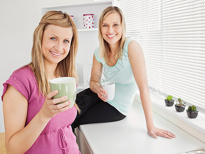 两个快乐的女人在家里拿着咖啡的肖像图片