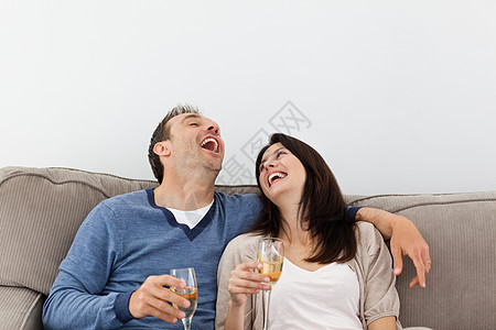 在沙发上喝香槟时笑着的情侣图片